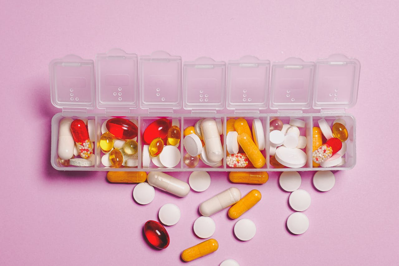A variety of pills in a weekly pill organizer on a pink background.