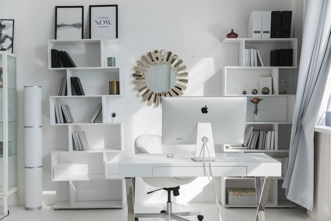 Bright minimalist home office setup with white shelves, desk, and iMac. Ideal for productivity.